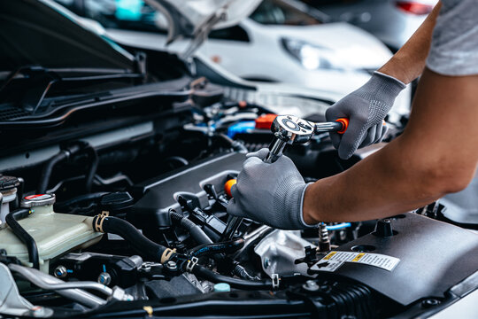 Mechanic using a spray tool on a car engine inside a workshop.