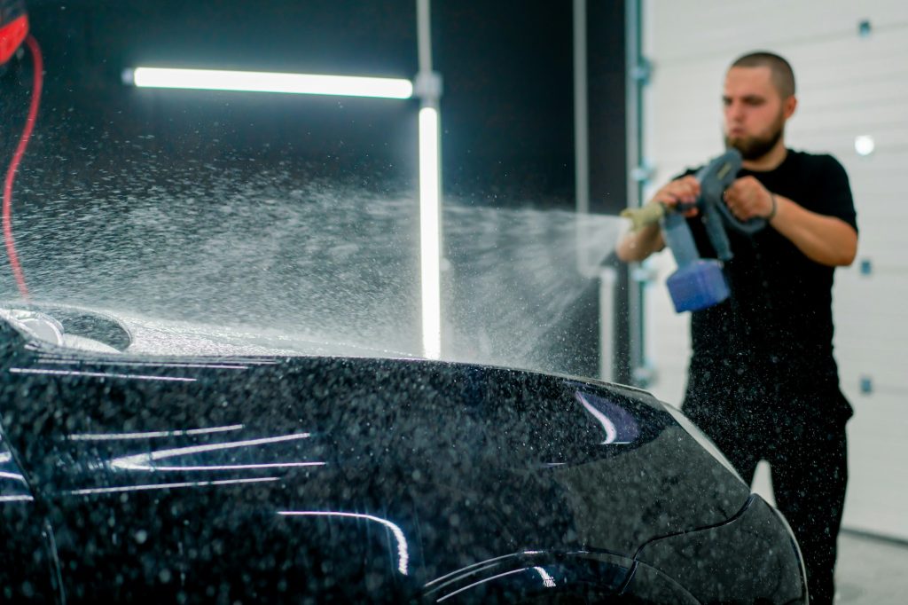 A person spray-painting a black car in a workshop.