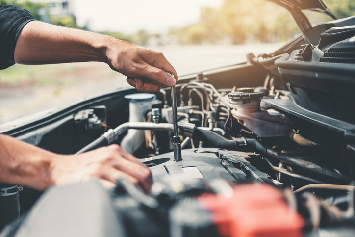 Hands working on a car engine under the hood.